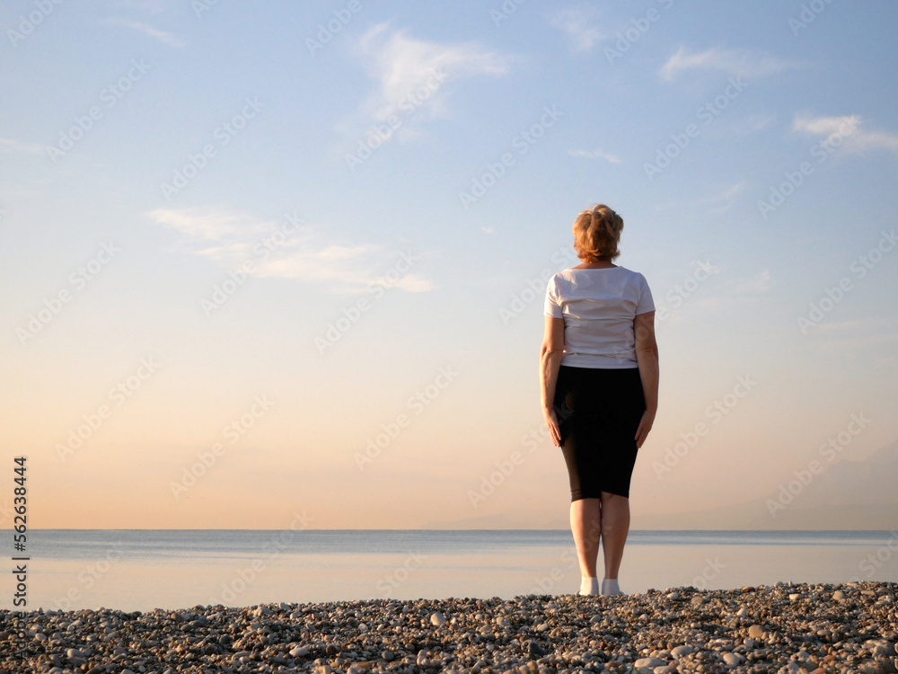 Senior 60s woman resting  alone on sea beach in sunset in sunny day, with copy space
