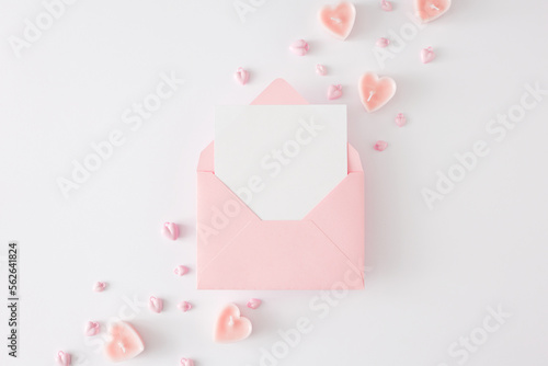 Valentines Day celebration concept. Top view composition made of pink heart shaped candles on white background and envelope with letter in the middle. Lovers holiday card idea.