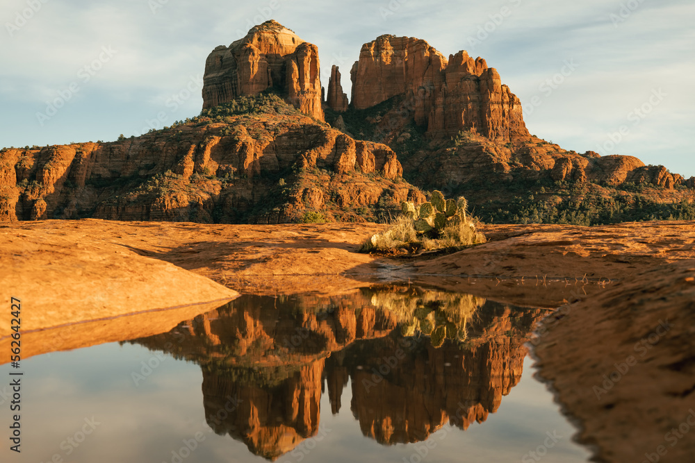 Horizontal image of cathedral rock seen from secret slickrock with reflection of geological sandstone rock formations and spires with cactus and water