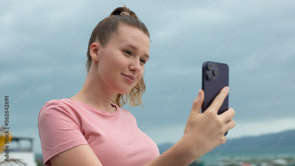 happy young girl uses her phone on the roof of a house, balcony, city background, woman taking selfie at summer, have a video chat, smiling have fun, photo of herself on mobile phone, smartphone 