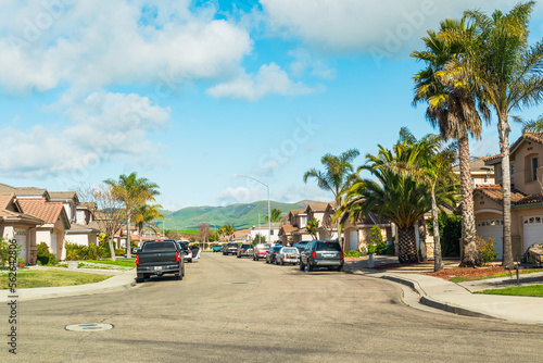 Beautiful houses with nicely landscaped front the yard, and cars parked on a sidewalk in small town in California. © Hanna Tor