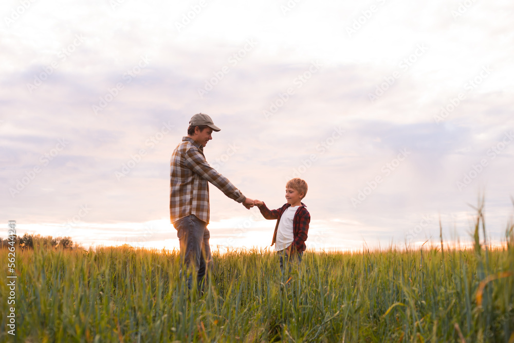 Farmer and his son in front of a sunset agricultural landscape. Man and a boy in a countryside field. Fatherhood, country life, farming and country lifestyle concept.