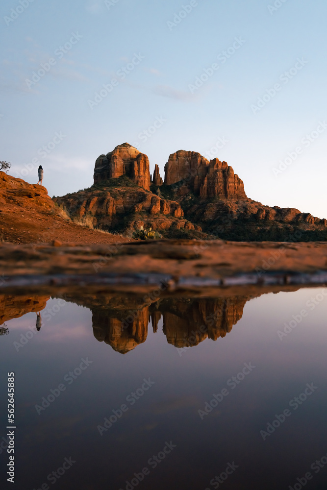 Young beautiful woman standing on rock point looking out at Cathedral Rock in Sedona Arizona USA Southwest at sunset with reflection from small pool.
