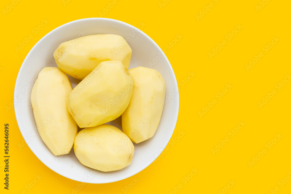 Raw peeled potatoes in white plate on yellow background.