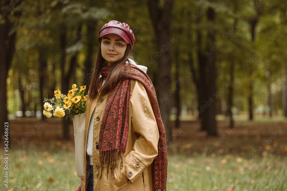 Young smiling woman with flowers in bag standing in autumn park and looking at camera Young smiling woman with flowers in bag standing in autumn park and looking at camera
