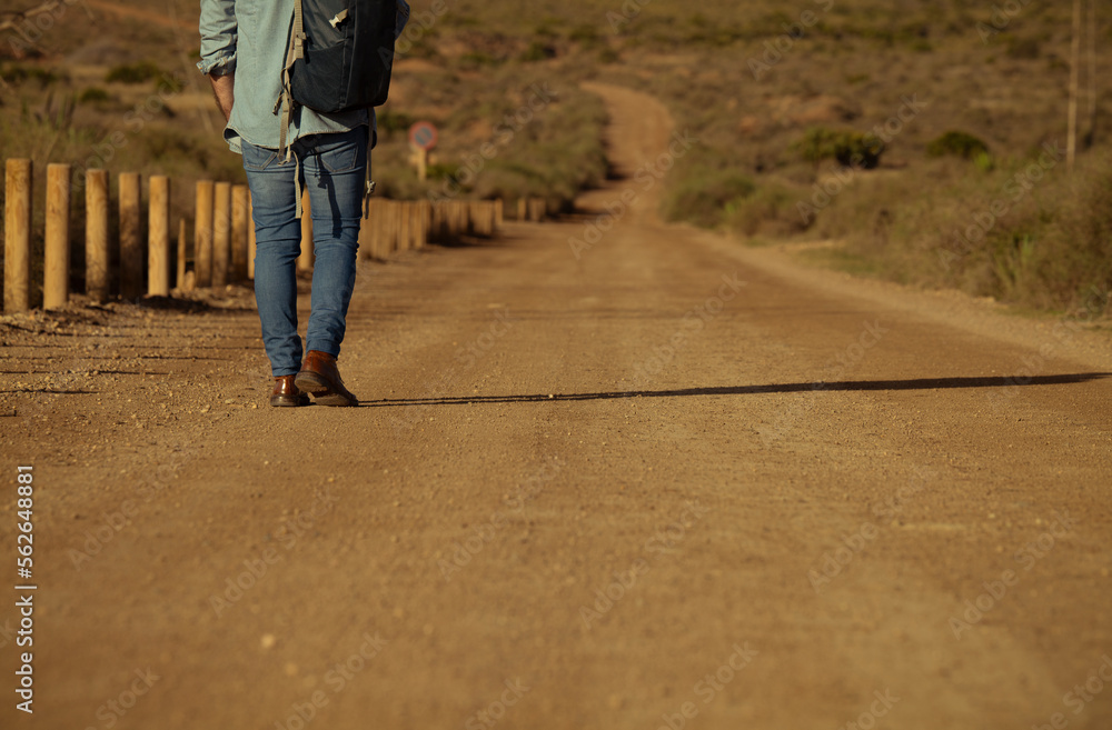 Adult man with backpack walking on dirt road