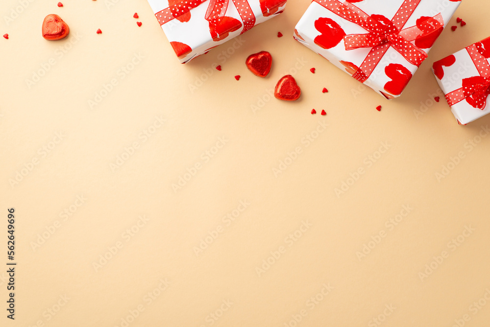 Valentine's Day concept. Top view photo of white gift boxes with ribbon bows heart shaped candies and sprinkles on isolated pastel beige background with copyspace Valentine's Day concept. Top view photo of white gift boxes with ribbon bows heart shaped candies and sprinkles on isolated pastel beige background with copyspace