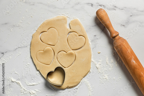 Cutting out heart shaped cookies from rolled out shortbread dough on marble table dusted with flour