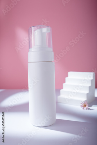 White dispenser mockup on pink backdrop in harsh light  no brand template. Cleansing facial foam container with flower and concrete stairs