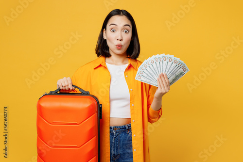 Young woman in summer casual clothes hold in hand fan of cash money dollar isolated on plain yellow background. Tourist travel abroad in free spare time rest getaway. Air flight trip journey concept #562660273