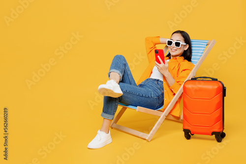 Photographie Young fun woman wear summer clothes sit in deckchair use mobile cell phone isolated on plain yellow background