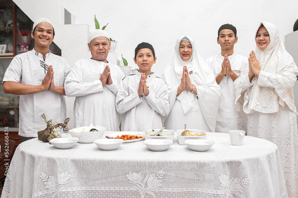 Group of happy family muslim gesturing hands apologize and welcoming in front of indonesian special food for the Eid Mubarak ramadan celebration. Group of happy family muslim gesturing hands apologize and welcoming in front of indonesian special food for the Eid Mubarak ramadan celebration.