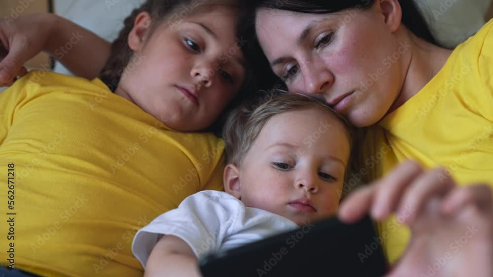 Happy family concept. Mom, daughter and son are play on bed. Child watching video on smartphone. Family leisure at home. Boy and girl with mom are watching movie on smartphone. Home education concept Happy family concept. Mom, daughter and son are play on bed. Child watching video on smartphone. Family leisure at home. Boy and girl with mom are watching movie on smartphone. Home education concept
