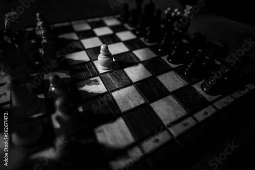 Blurred black and white background with a low depth of focus. The set of wooden chess pieces elements standing on chess board on dark background.