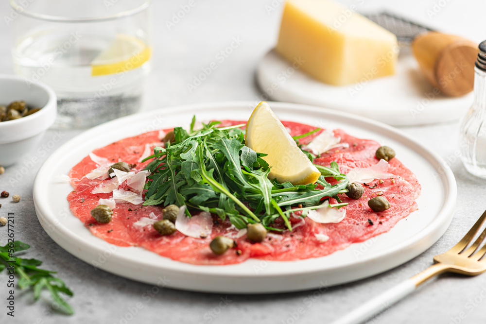 Beef carpaccio with capers, arugula and parmesan on a white plate, selective focus Beef carpaccio with capers, arugula and parmesan on a white plate, selective focus