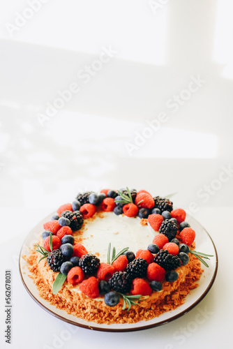Homemade cake with fresh berries on top on a white wall background