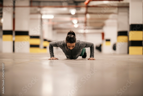 Strong bodybuilder is doing pushups in underground garage.