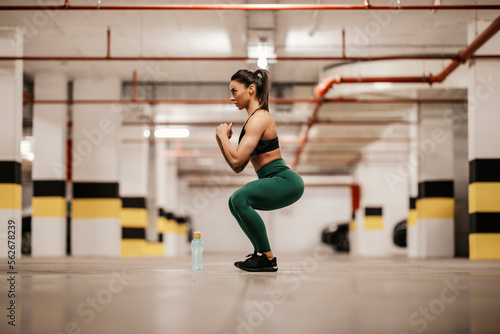 Side view of a sportswoman doing squat endurance in underground garage.