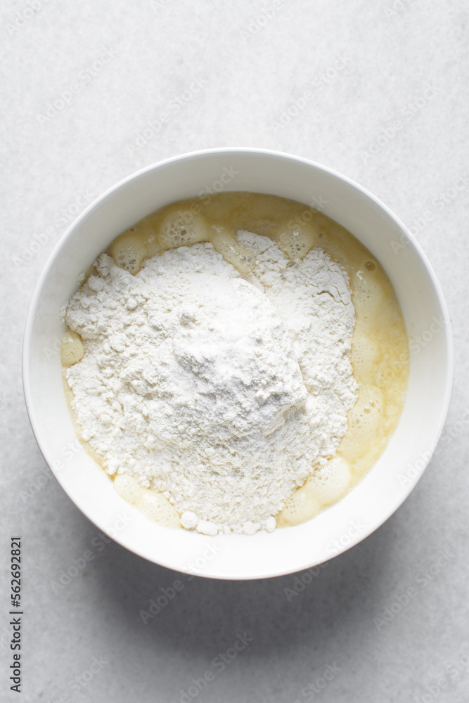 All purpose flour in a white bowl with milk and egg mixture