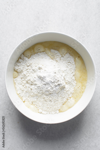 All purpose flour in a white bowl with milk and egg mixture