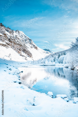 Picturesque landscape of a snowy winter mountain lake. Small lake next to the Saut Deth Pish waterfall during autumn and a snowy day, located in the Aran Valley, Pyrenees, Catalonia, Spain.