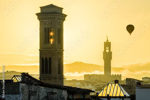 The rising sun over the Florence cityscape with the sunstars in the tower of the Chiesa di San Salvatore in Ognissanti and the flying balloon above the Palazzo Vecchio in the autumn morning. photo