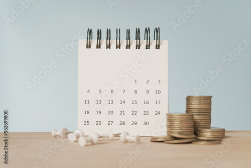 For payday loan concept. White calendar and blurred stack of coins , blurred white thumbtack on wood desk photo