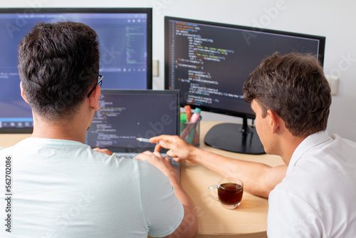 Two young programmers work on a programming project on a modern desktop computer with three monitors © Anderson Piza