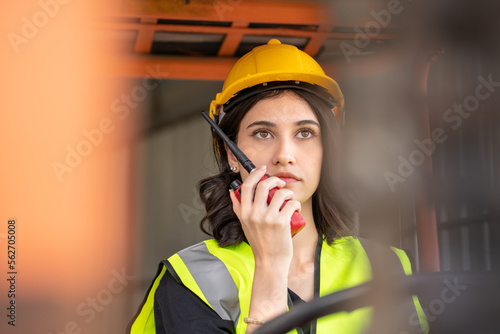 Obraz na płótnie Female foreman using radio while driving forklift vehicle at shipping warehouse