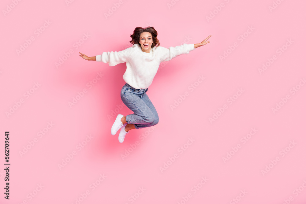 Full length photo of shiny adorable lady wear white sweater jumping high arms sides isolated pink color background