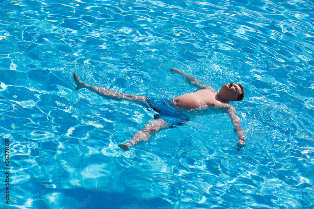 An adult large man swims on his back pool with clear blue water.