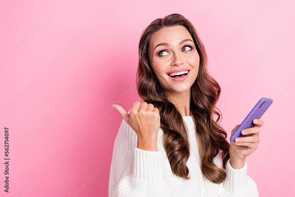 Photo of gorgeous cheerful person hold telephone look direct finger empty space isolated on pink color background Photo of gorgeous cheerful person hold telephone look direct finger empty space isolated on pink color background