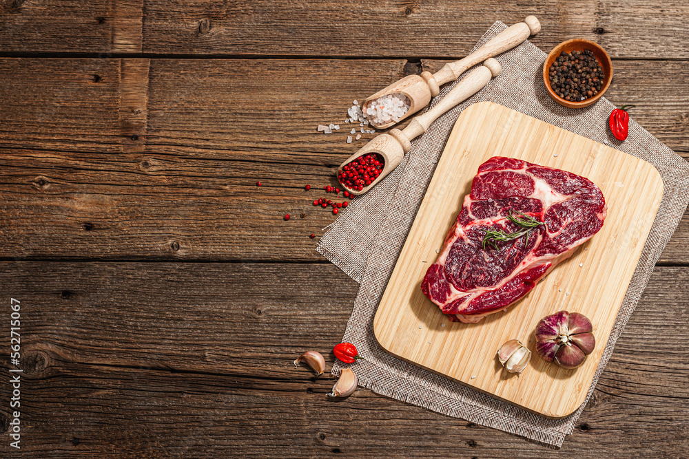 Raw Ribeye steak with spices and herbs. Dry aged meat, traditional food, hard light, dark shadow Raw Ribeye steak with spices and herbs. Dry aged meat, traditional food, hard light, dark shadow