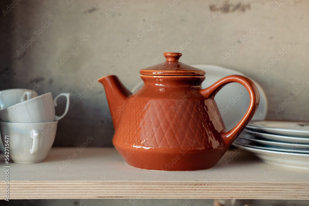 brown clay teapot on a white shelf with cups and plates brown clay teapot on a white shelf with cups and plates