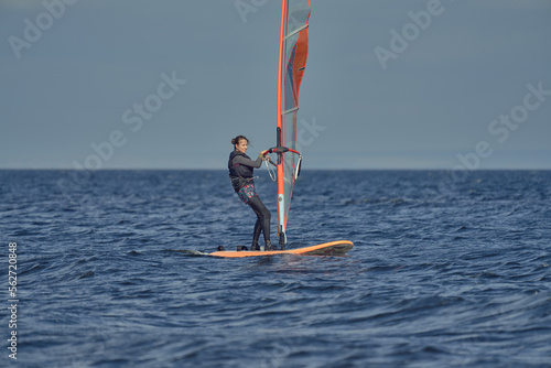 Mature woman beginner windsurfer moves slowly on a sailboard on a sunny autumn day.