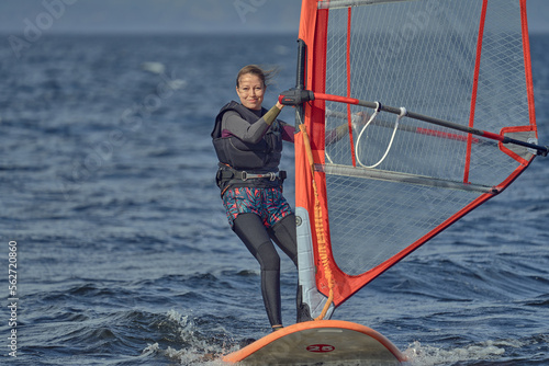 Mature woman beginner windsurfer moves slowly on a sailboard on a sunny autumn day.
