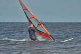 A mature man in a wetsuit, a windsurfer, slows down a sailboard, finishes moving on the water on a sunny autumn day.
