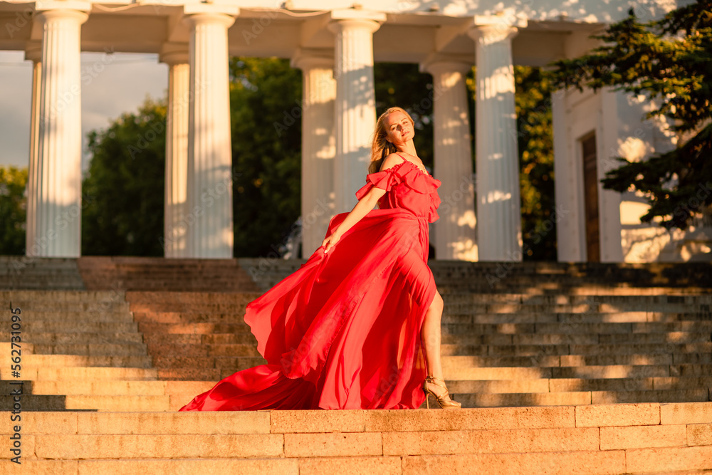 A woman in a long red dress against the backdrop of sunrise, bright golden light of the sun's rays. The concept of femininity, harmony.