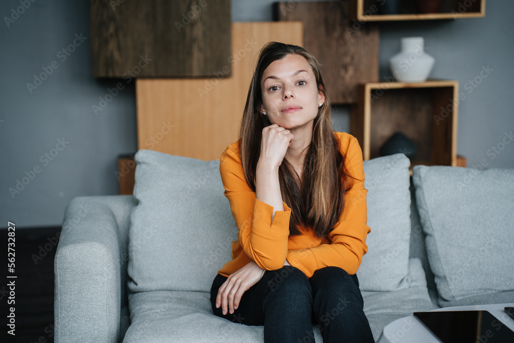 Disappointed brunette hispanic woman in orange blouse sitting on cozy ...