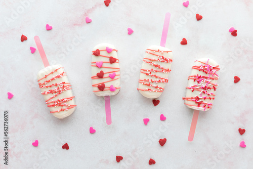 Valentine's Day cakesicles with sprinkles on a pink marble surface. photo