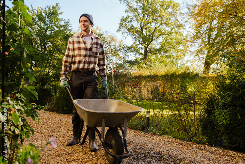 Fotografering Young man walking with wheelbarrow while working in garden