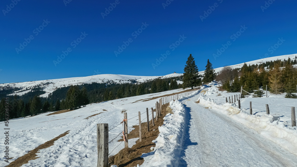 Snow covered hiking trail along alpine fence on the way to mountain peak Ladinger Spitz, Saualpe, Lavanttal Alps, border Styria Carinthia, Austria, Europe. Ski tour, snow shoeing on a sunny winter day