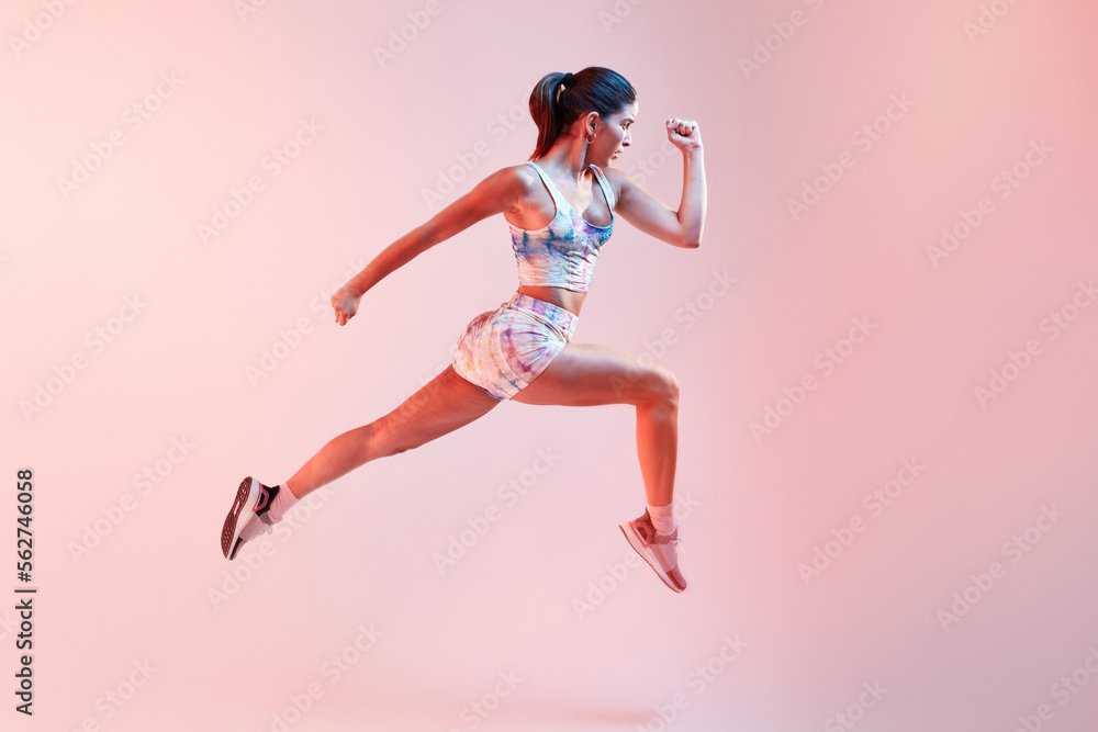 Stylish sportswoman jumping on pink background Stylish sportswoman jumping on pink background