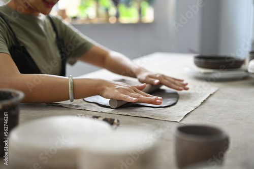 Close up and cropped image with Woman potter master rolling with pin while preparing clay mug, production process of handicrafter pottery. Ceramic making concept. photo