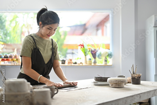 Portrait with Woman potter master rolling with pin while preparing clay mug, production process of handicrafter pottery. Ceramic making concept. photo