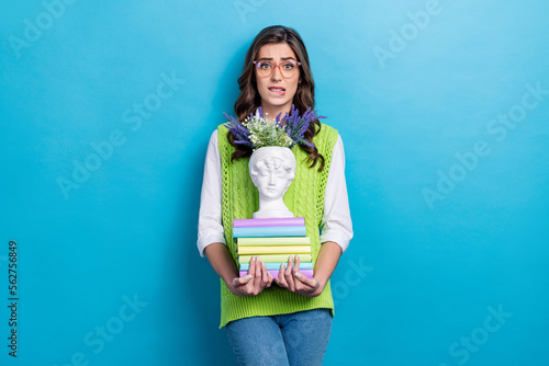 Photo portrait of lovely young lady specs nervous fired hold stack book statue wear trendy green garment isolated on blue color background