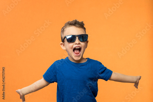 Portrait of surprised cute little toddler boy in sunglasses. Child with open mouth having fun isolated over orange background. Looking at camera. Wow funny face
