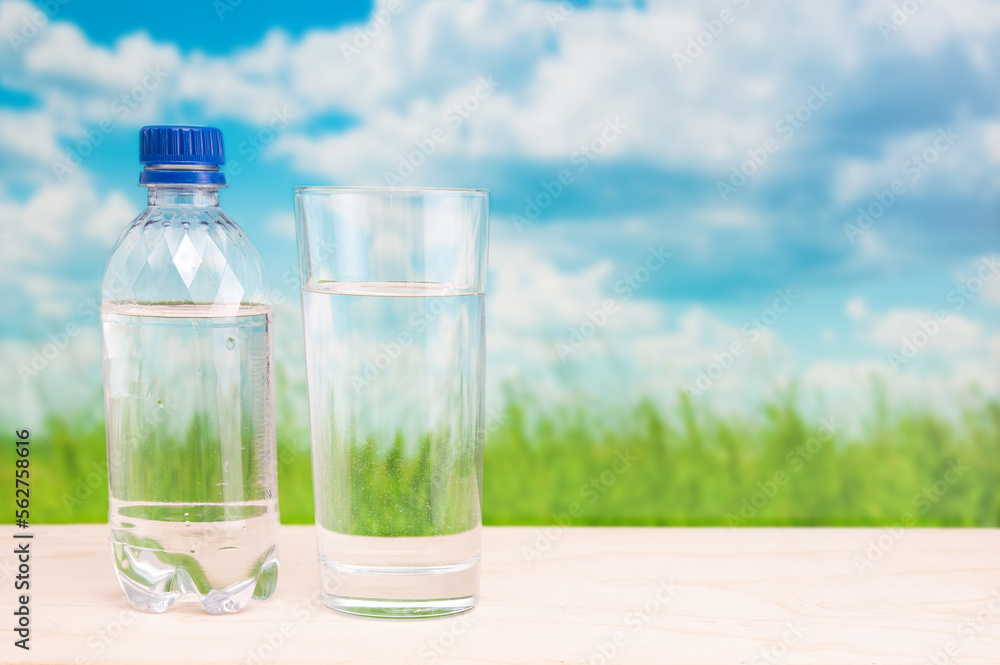Plastic bottle and glass with pure water on grassland landscape background Plastic bottle and glass with pure water on grassland landscape background