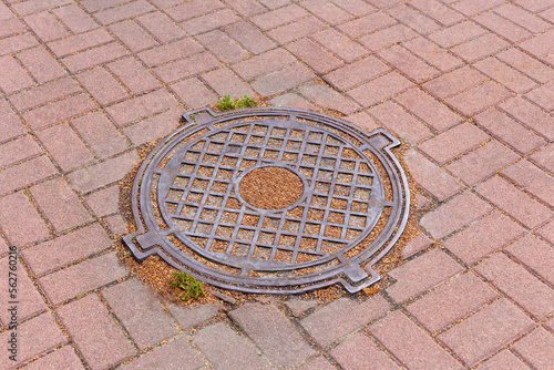 Iron sewer manhole on the ground among the tiles close-up