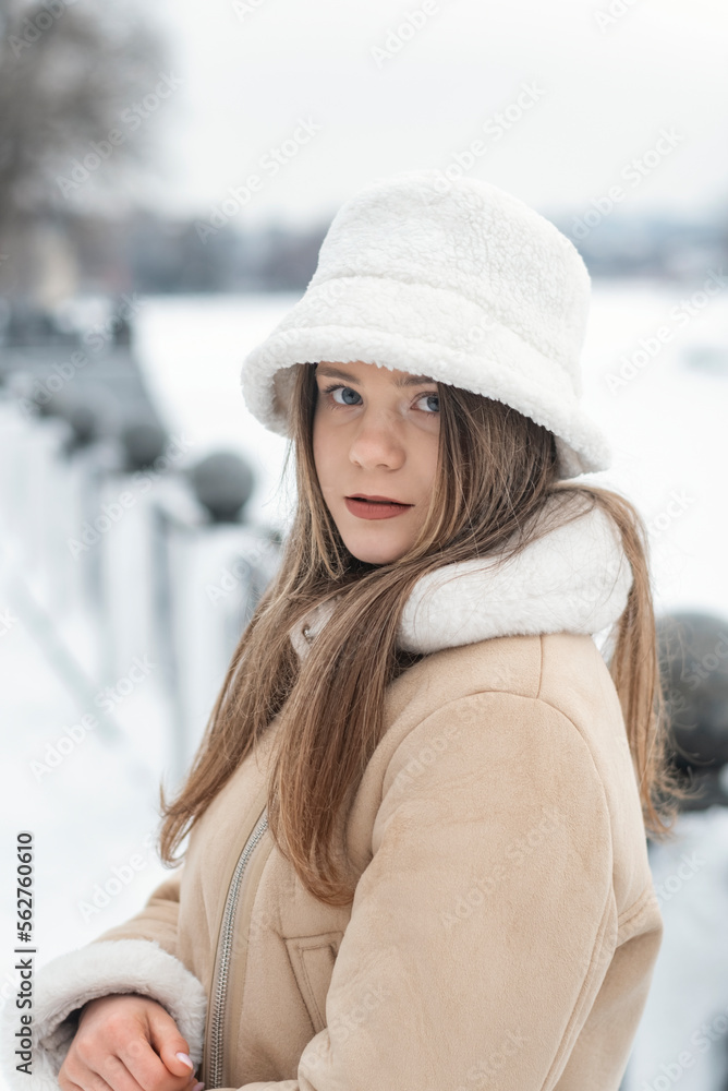 Portrait of stylish girl in white fur panama and beige sheepskin coat outside in winter. Fashionable warm womens clothing Portrait of stylish girl in white fur panama and beige sheepskin coat outside in winter. Fashionable warm womens clothing